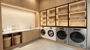 Una sala de lavandería con cuatro lavadoras, armarios de madera y estantes de almacenamiento.