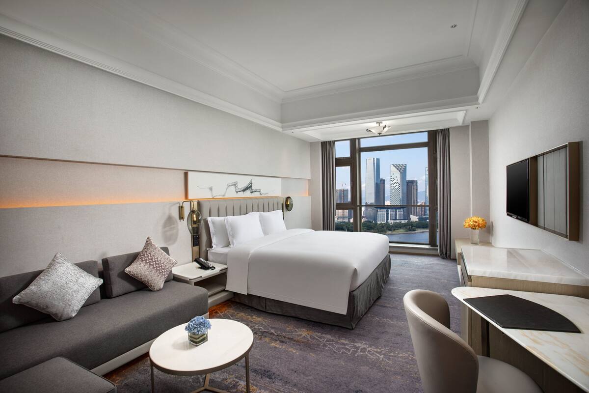 Ein modernes Hotelzimmer mit einem großen Bett, einer Couch, einem Schreibtisch und Blick auf die Stadt.