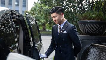 A man in a dark pinstripe suit with a tie and white gloves opening a car door.