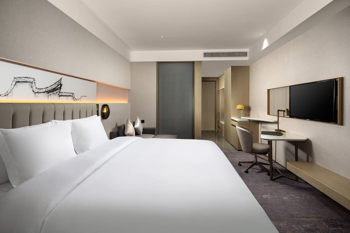 Ein Hotelzimmer mit einem großen Bett, einem Schreibtisch, einem Sessel, einem Fernseher und einem Wandbild.