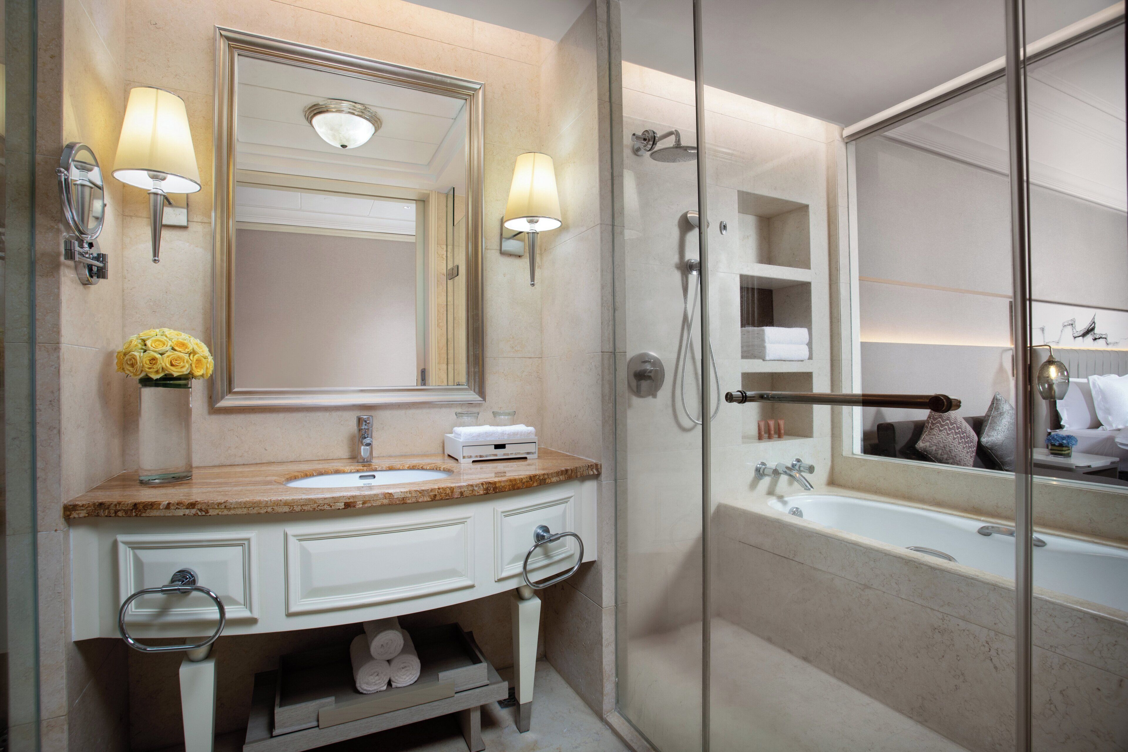 A bathroom with a marble sink, a large mirror, a glass-enclosed shower, and a towel rack.