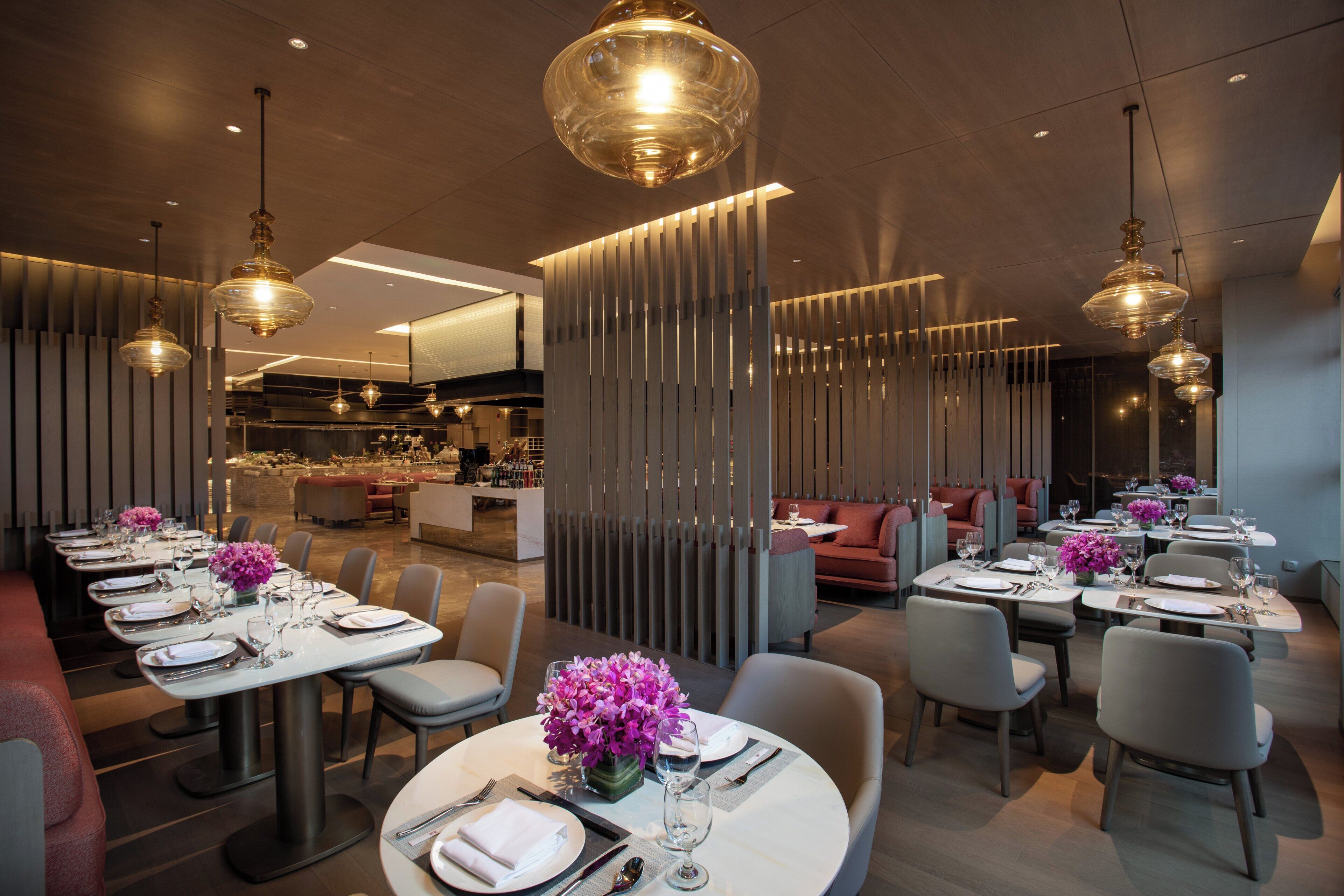 A modern restaurant interior with multiple dining tables, chairs, and pendant lighting.