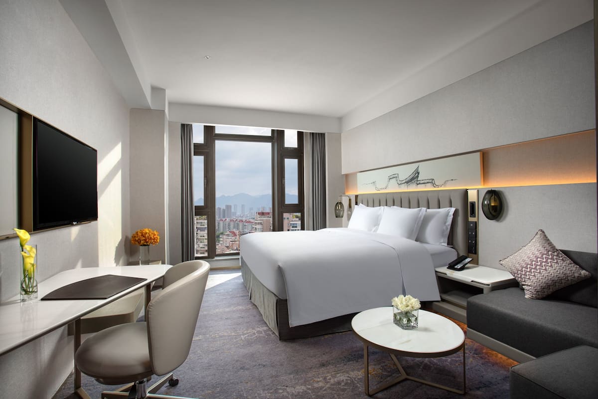 Ein modernes Hotelzimmer mit einem großen Bett, einem Schreibtisch, einem Sessel, einer Couch, einem kleinen Tisch und einem Fernseher.