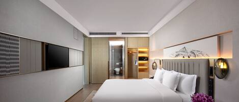 A modern hotel room with a large bed, a flat-screen TV mounted on the wall, a bedside table with a vase of flowers, and a walk-in closet.