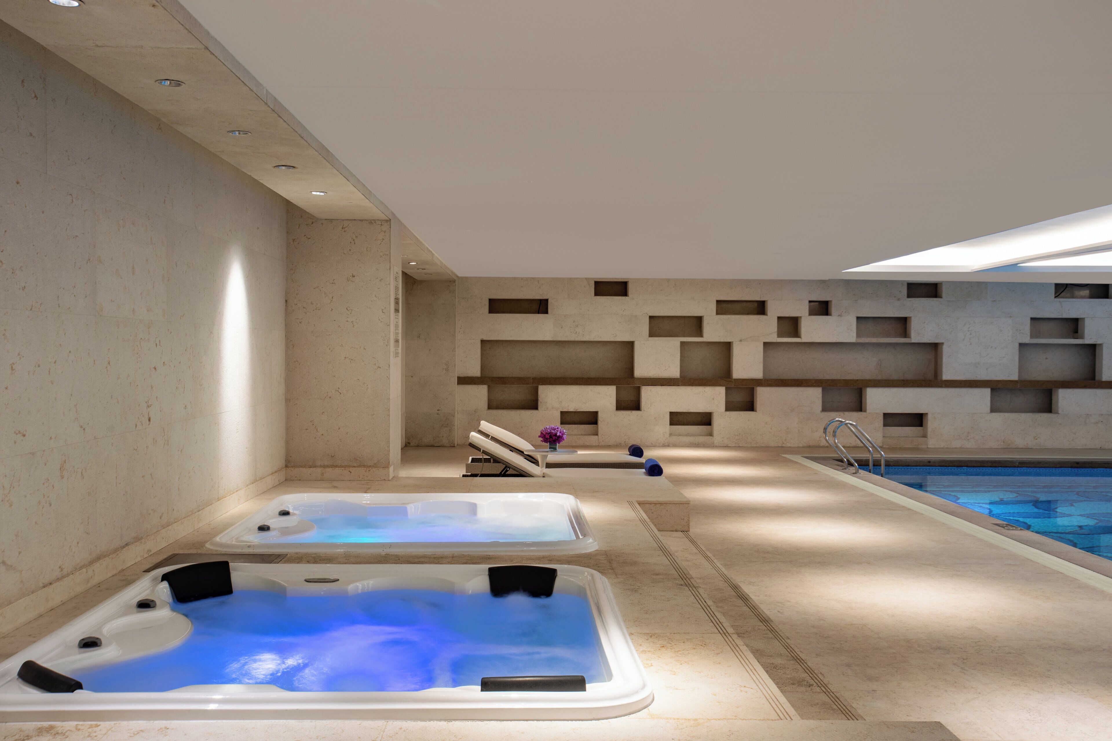 Ein Wellnessbereich mit zwei Whirlpools, einem Pool und einem modernen Wanddesign.