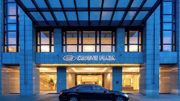 A hotel entrance with a car parked in front, a clear sky, and a sign reading 'CROWNE PLAZA'.