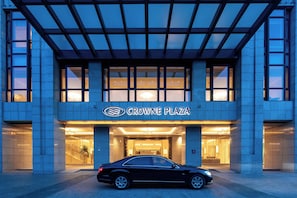 Et hotelindgangsparti med en bil foran, en klar himmel og et skilt der siger 'CROWNE PLAZA'.