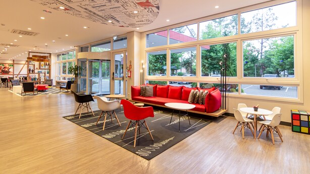 A modern interior with a red sofa, white chairs, and a small table. Large windows offer a view of the outdoors. - ibis Igrejinha (Igrejinha)