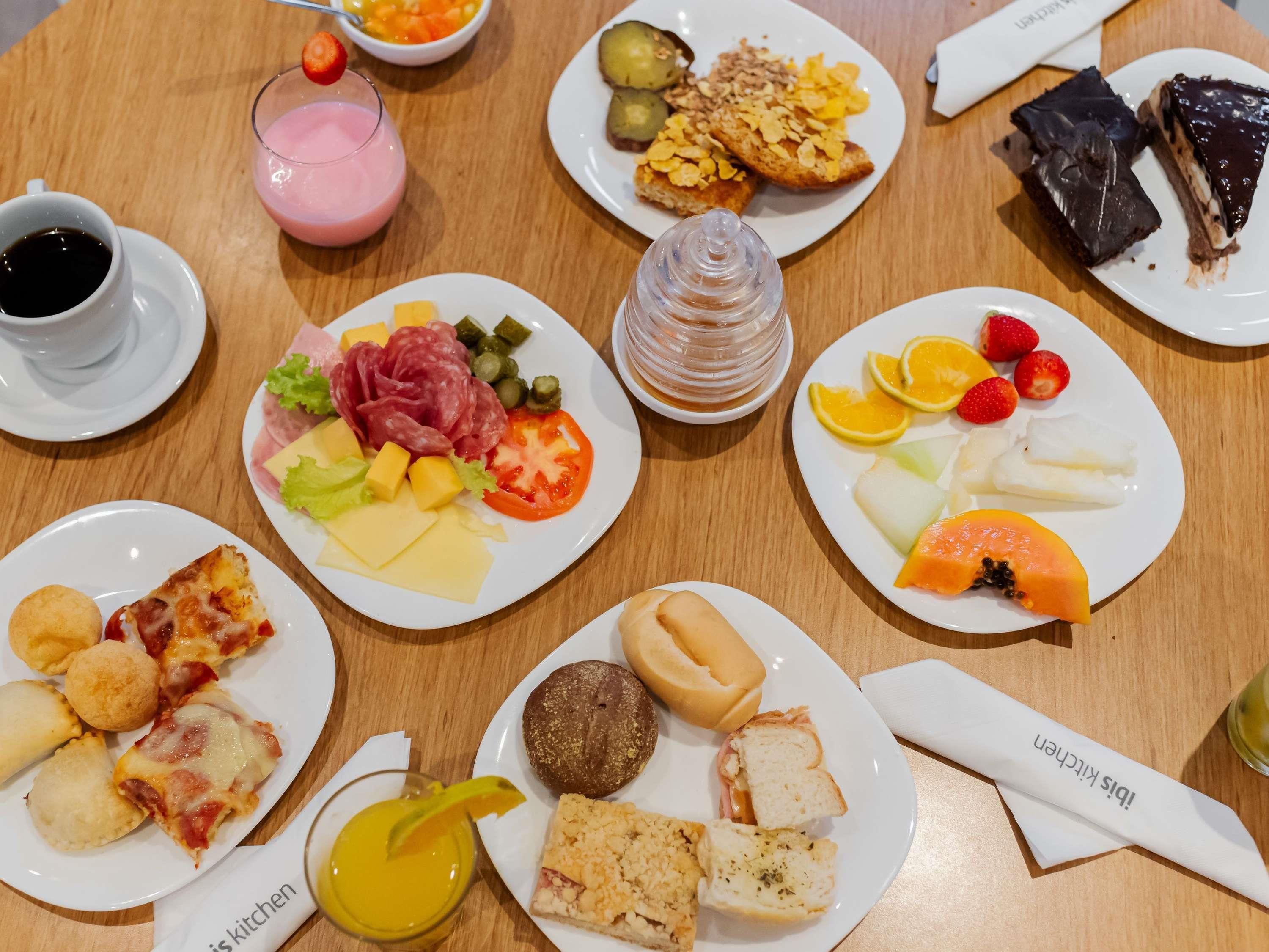 A variety of food items on a wooden table, including plates with different dishes, a glass of juice, and a cup of coffee.