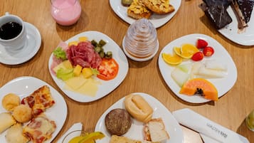 A variety of food items on a wooden table, including plates with different dishes, a glass of juice, and a cup of coffee.