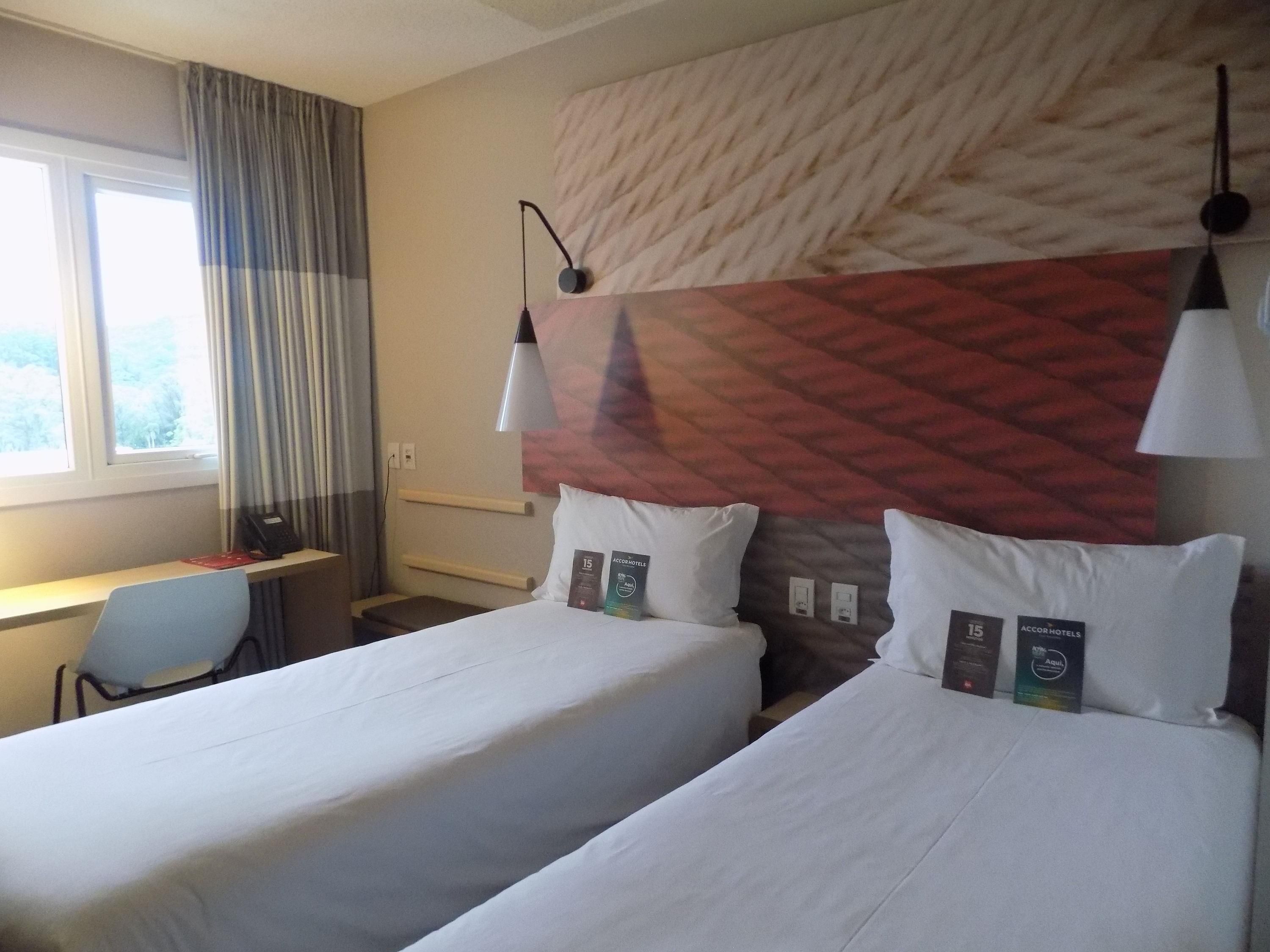 Una camera d'albergo con due letti, una scrivania e una finestra con tende.