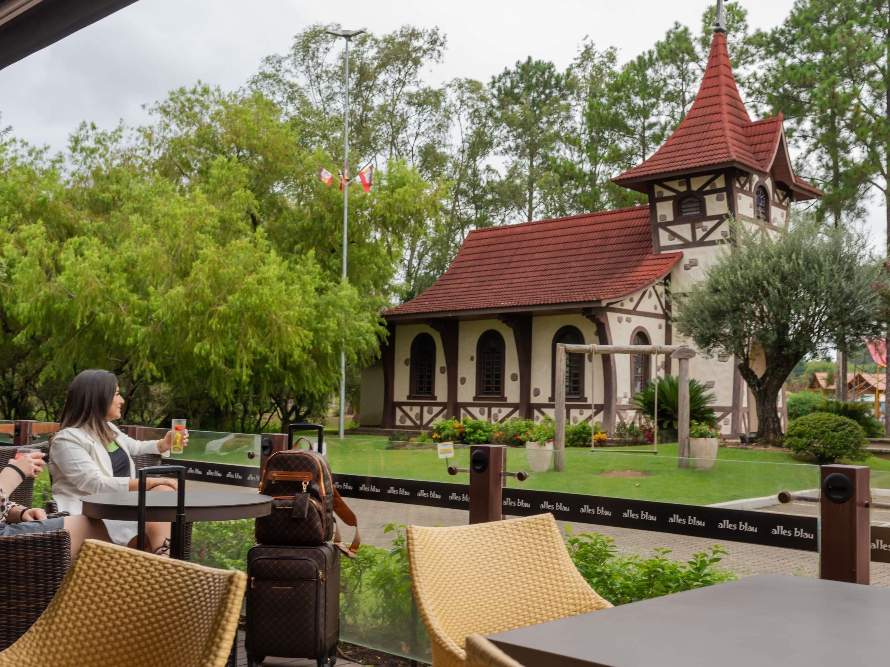 An outdoor seating area with wicker chairs and tables, a small building with a red roof, and a flagpole with flags.