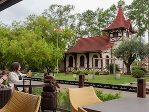 An outdoor seating area with wicker chairs and tables, a small building with a red roof, and a flagpole with flags. - ibis Igrejinha (Igrejinha)