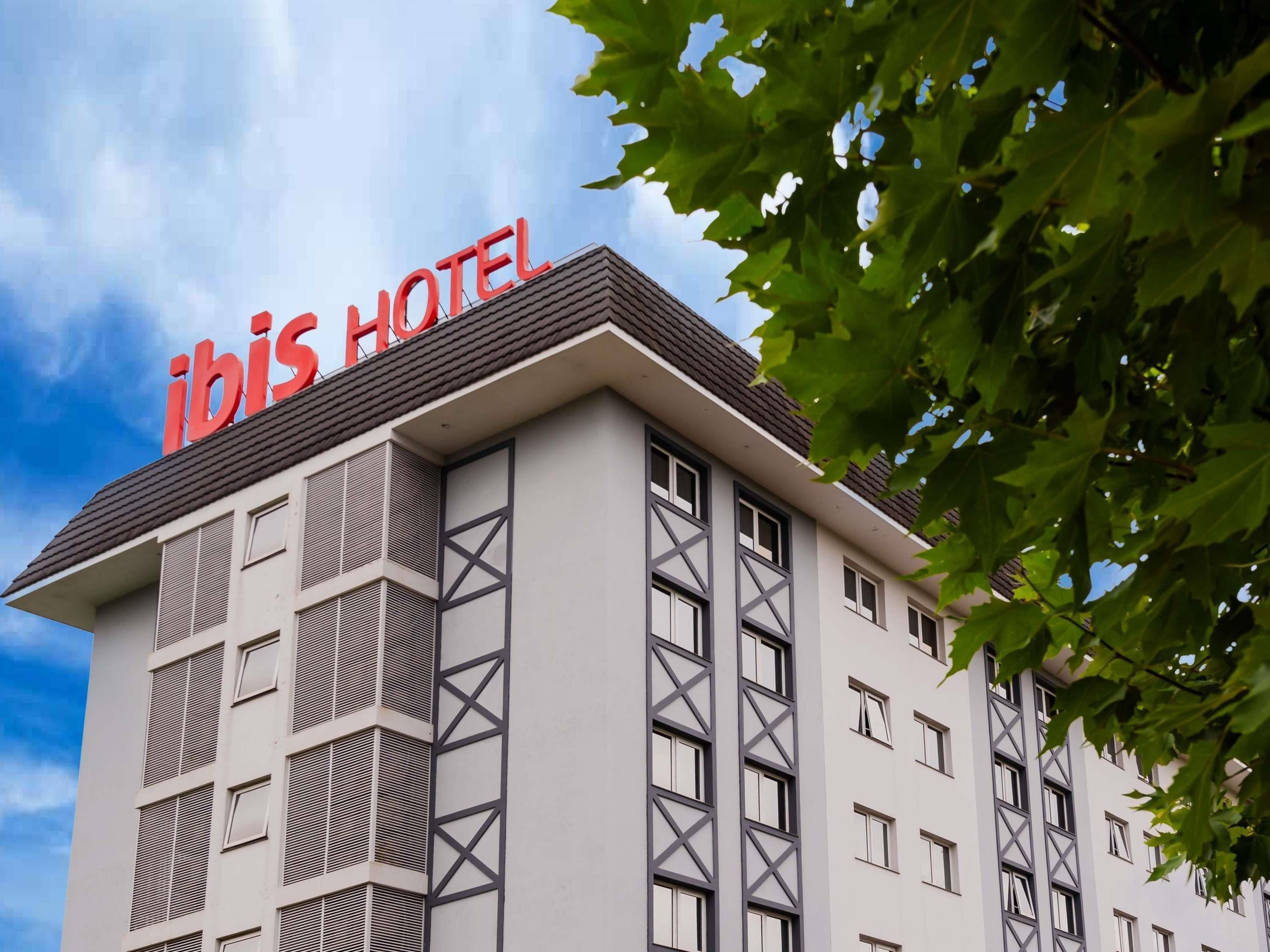 A hotel building with a prominent 'ibis HOTEL' sign on top, featuring a modern architectural design with a flat roof and a series of windows.