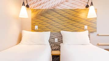 A hotel room with two single beds, a headboard with a textured pattern, and two wall-mounted reading lamps.