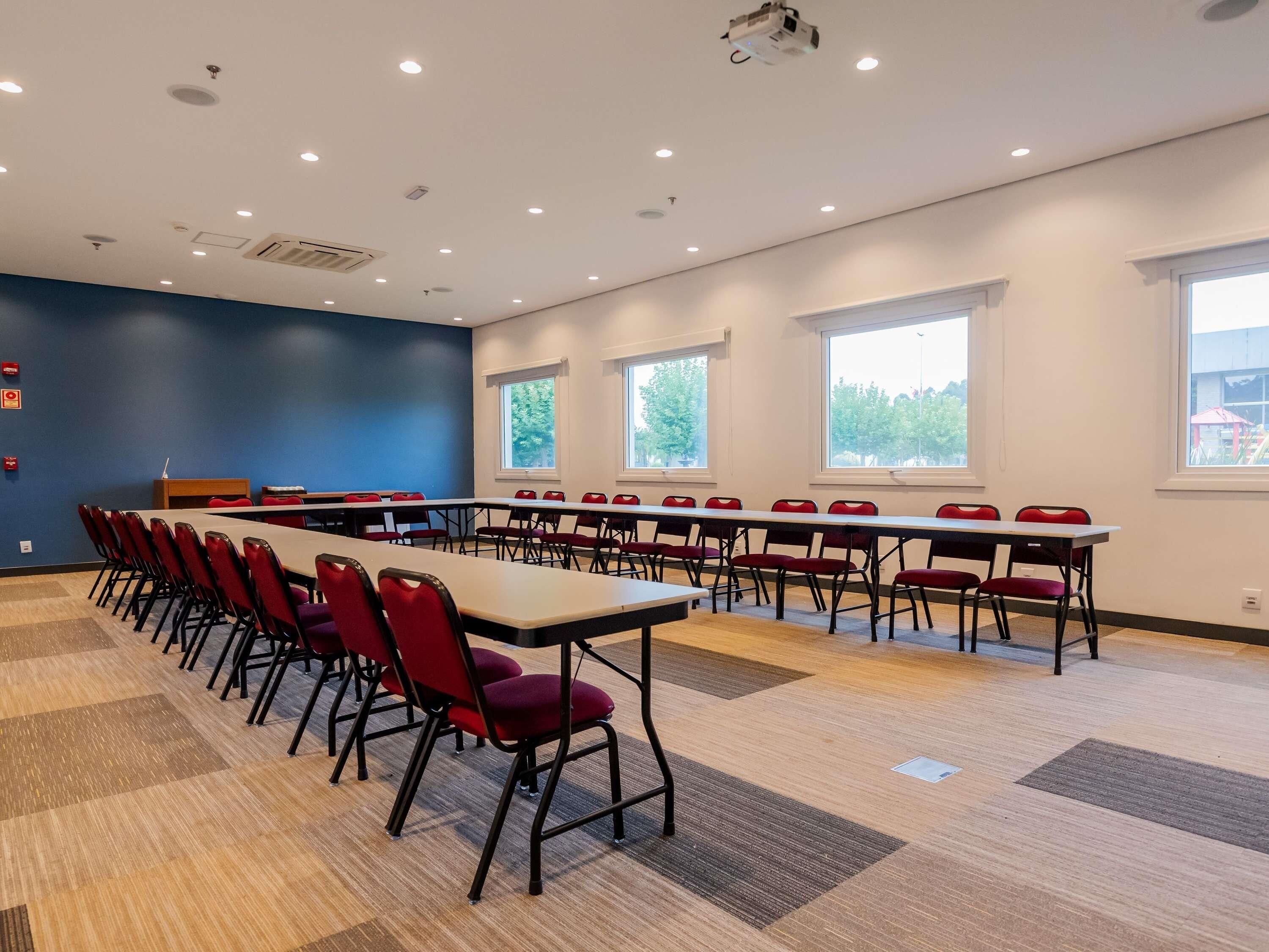 A conference room with multiple tables and chairs, large windows, and a projector on the ceiling.
