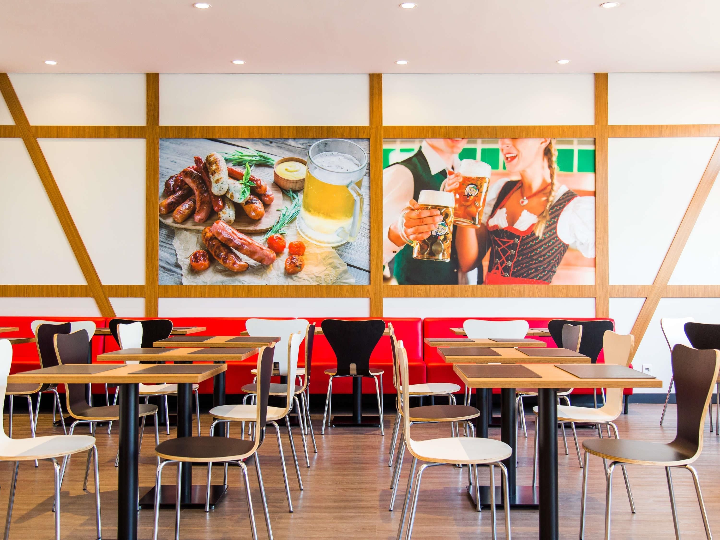 A restaurant with a modern interior, featuring wooden panel walls, red seating, and tables with metal chairs.