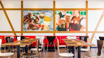 A restaurant with a modern interior, featuring wooden panel walls, red seating, and tables with metal chairs.