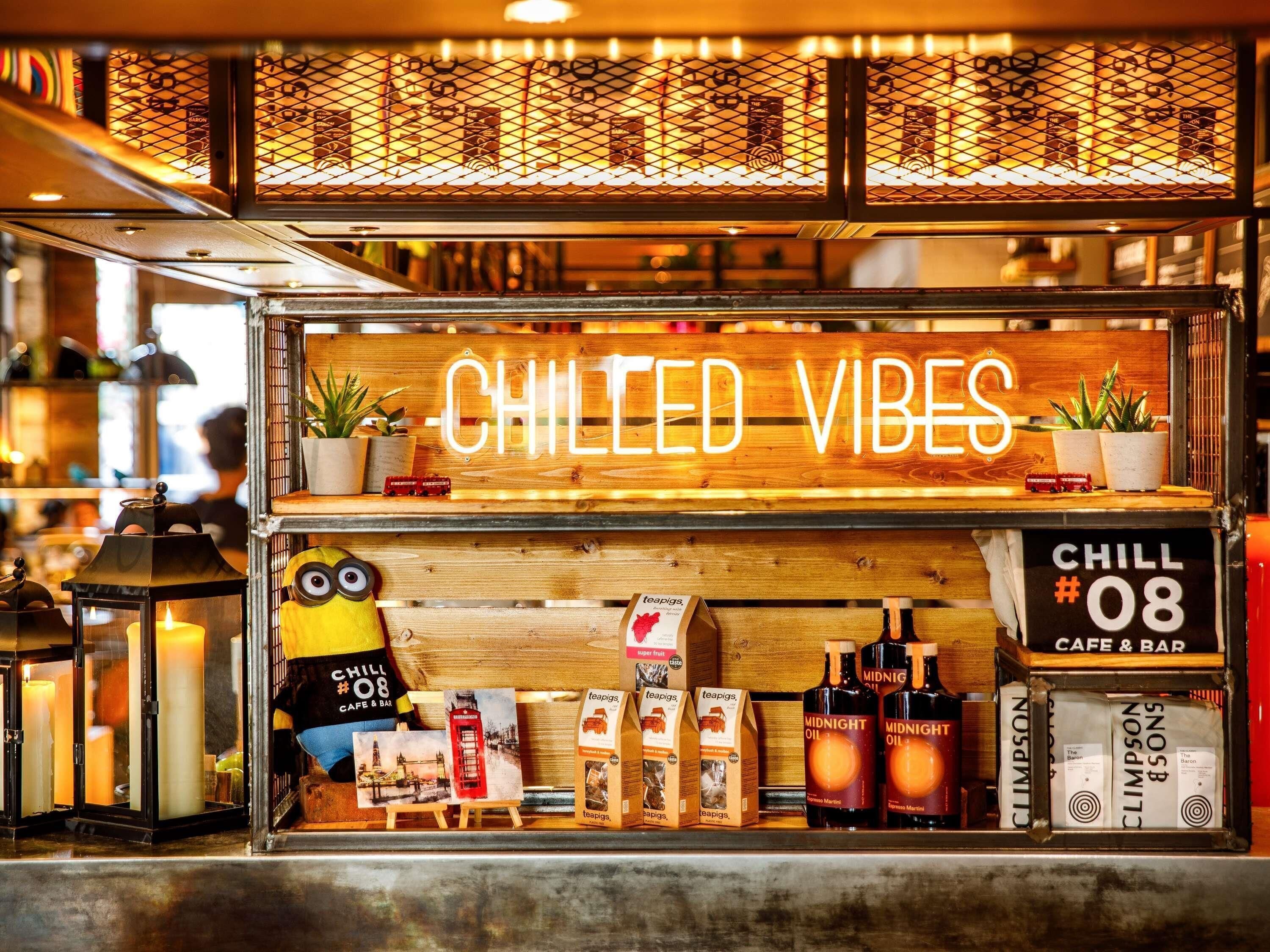 Un café con un letrero de neón que dice 'CHILLED VIBES' y un peluche de Minion. Se exhiben bolsitas de té teapigs y botellas de Midnight Oil.