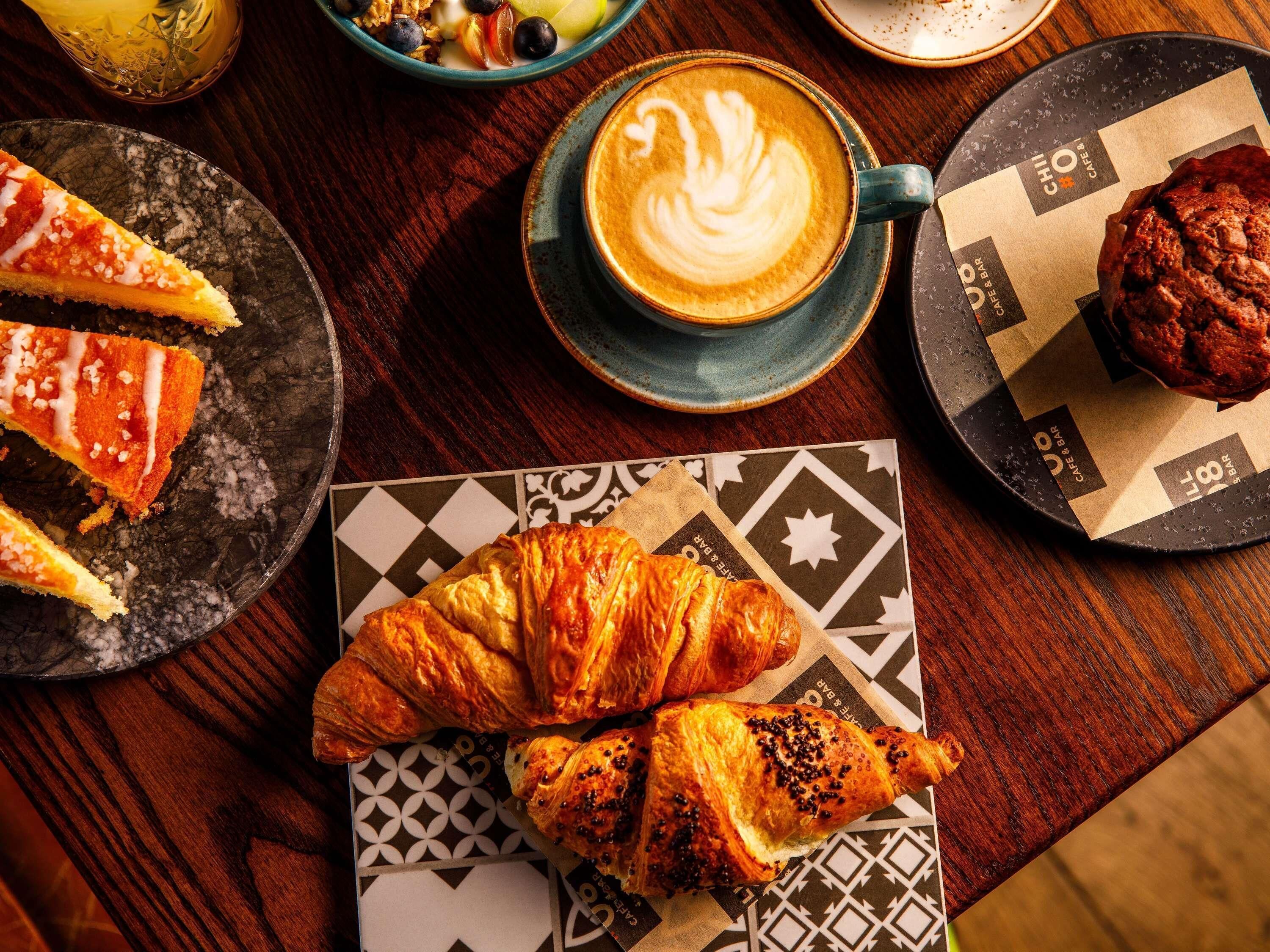 A table with a croissant, a slice of pie, a cup of coffee, and a muffin.