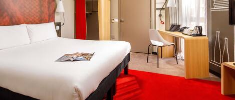 A hotel room with a bed, a desk, a chair, a red snowboard, and a TV.