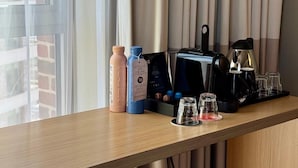A hotel room with a wooden desk, a coffee maker, two bottles, and a glass.