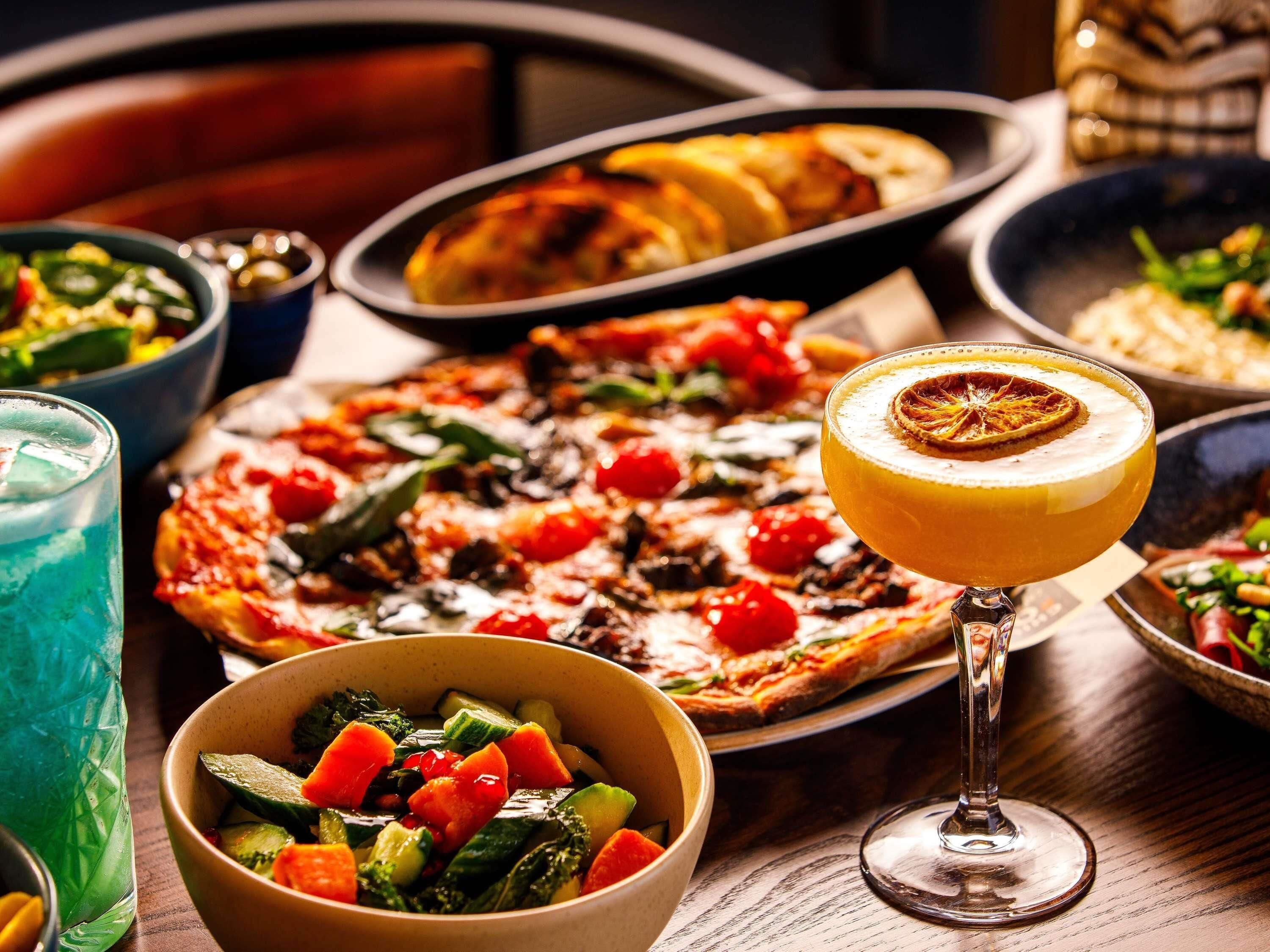 A table with a variety of dishes including pizza, a salad, and a drink with a garnish.