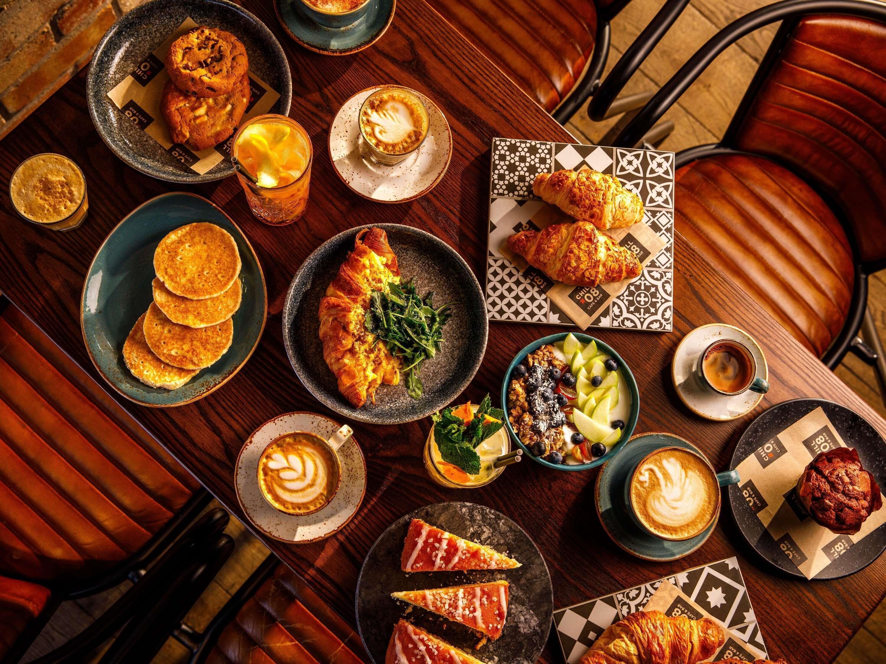 Une table sur laquelle on trouve divers aliments et boissons, notamment des pâtisseries, un croissant et un verre de café.