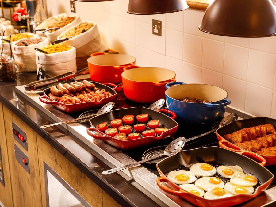 A buffet with various dishes including sausages, eggs, and tomatoes.