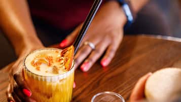 A person holding a glass with a straw, a candle, and a dessert item on a wooden table.