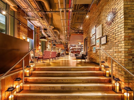 A staircase with wooden steps and lanterns, leading to a bar area with seating and a brick wall with a sunburst clock.
