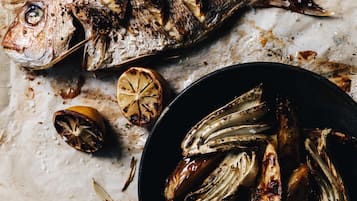 A roasted fish with lemon slices and grilled vegetables on a marble surface.
