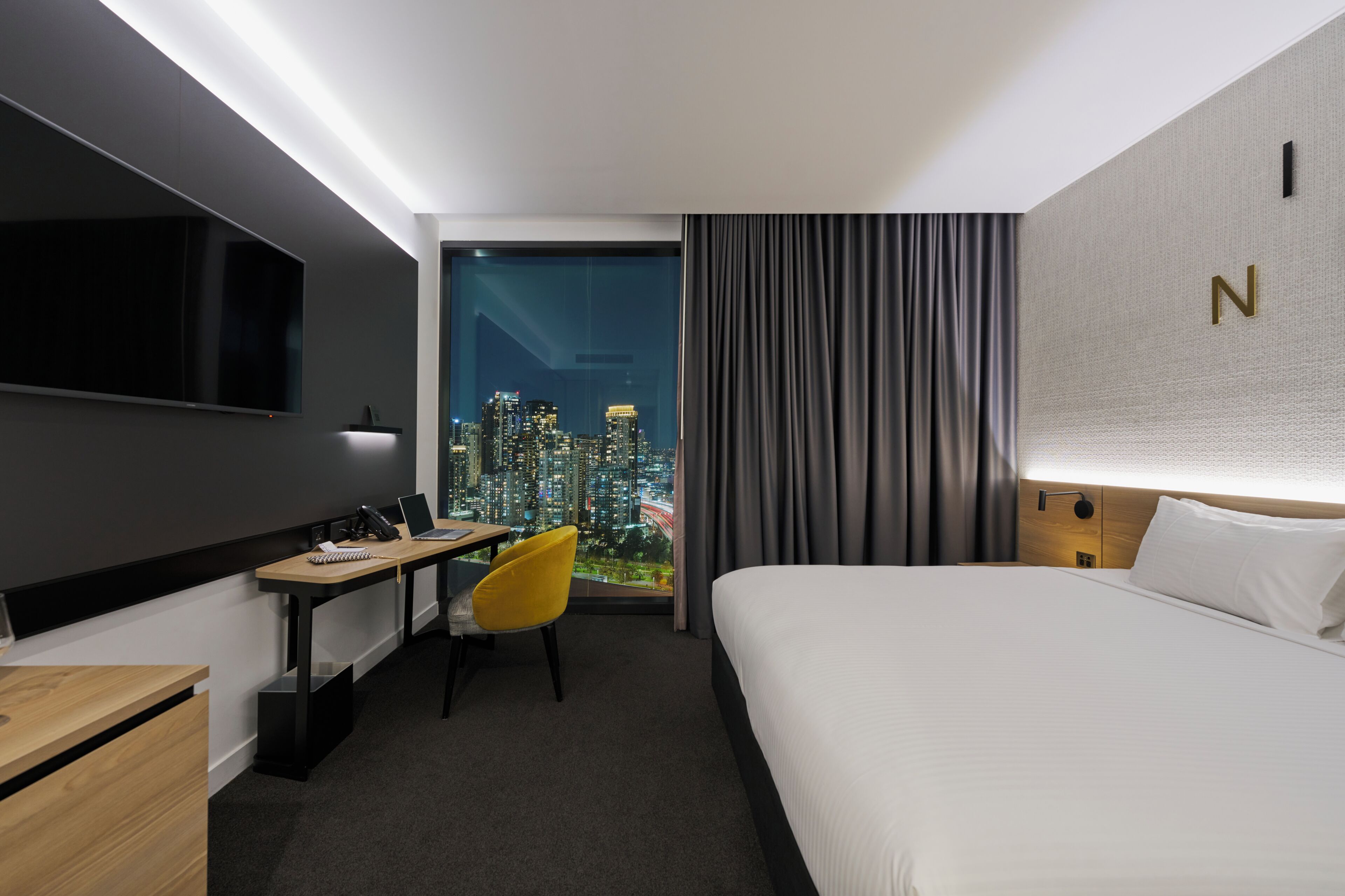 Habitación de hotel con cama, escritorio con silla, televisión y vista a la ciudad.