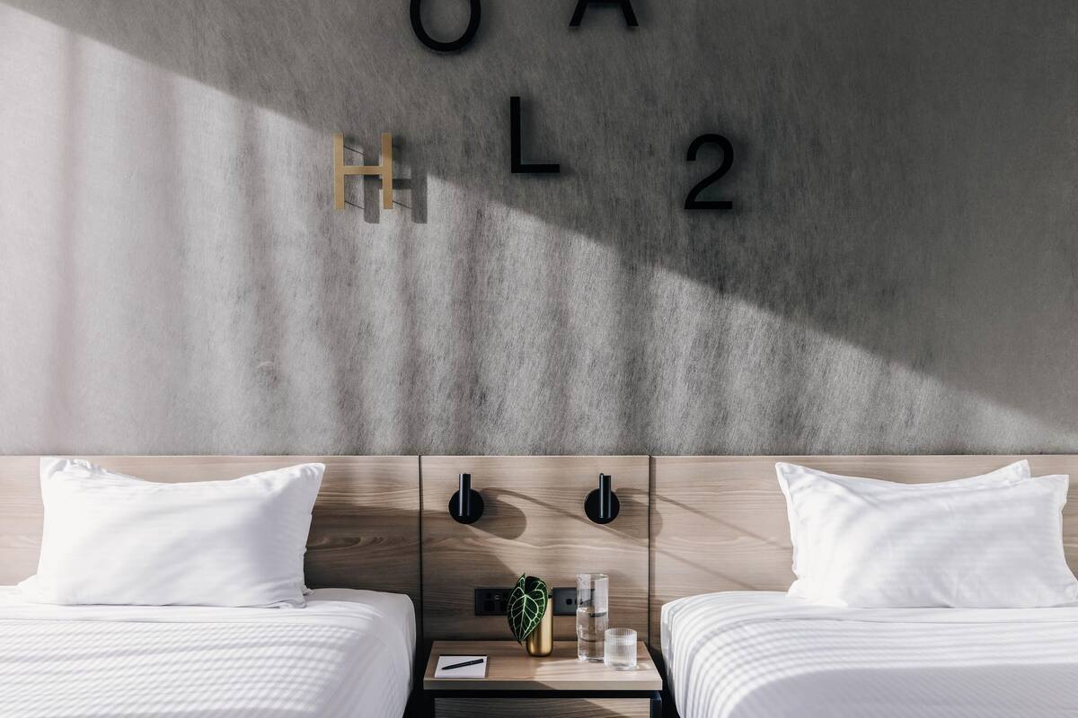 Ein modernes Hotelzimmer mit zwei Betten, einem Nachttisch mit Pflanze und einer Wand mit Buchstaben und Zahlen.