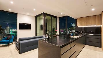 Una cocina moderna con una isla central, un área de comedor con sofá y un amplio ventanal con vista a la ciudad.