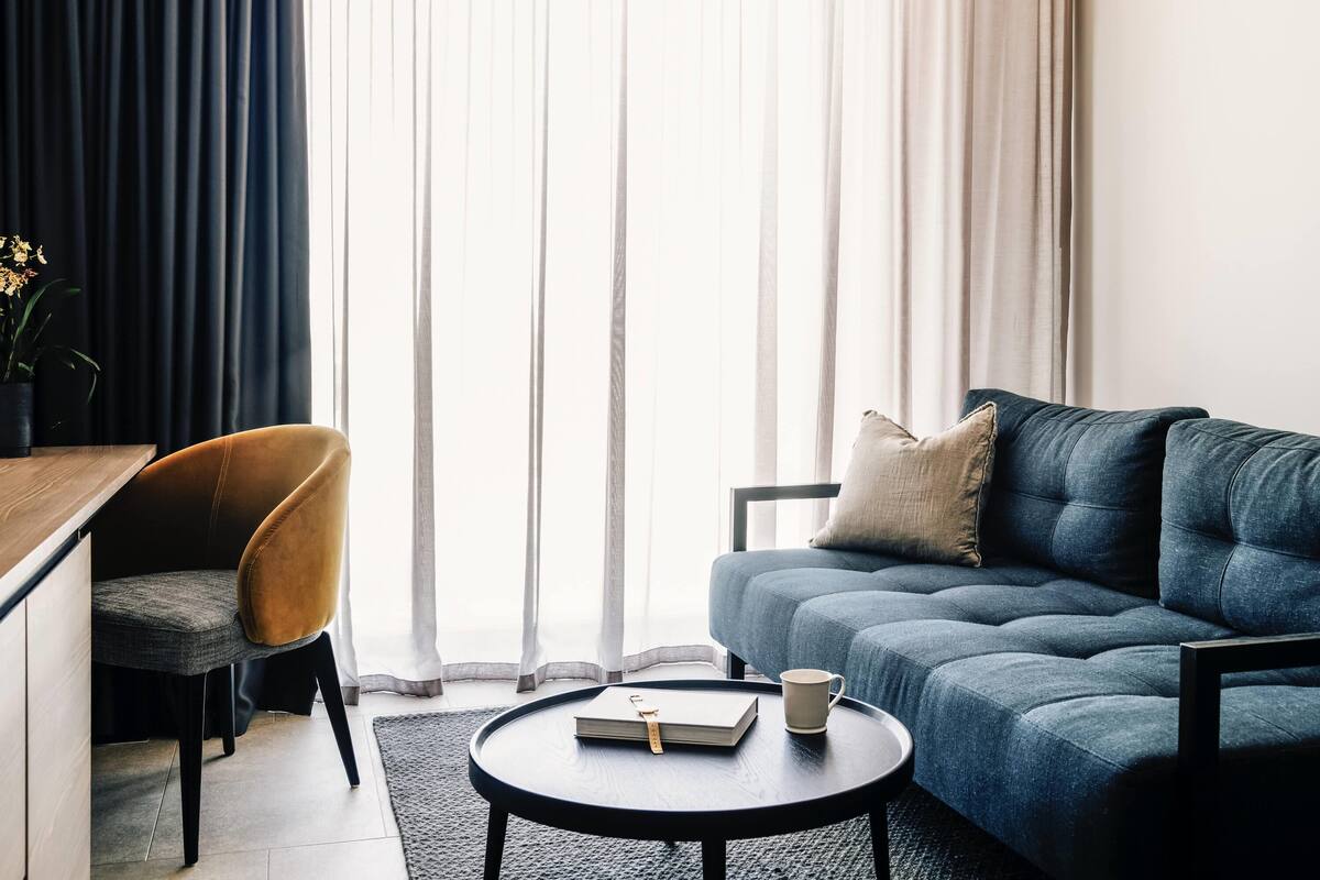 A modern living room with a sofa, a chair, a coffee table, and a view through sheer curtains.