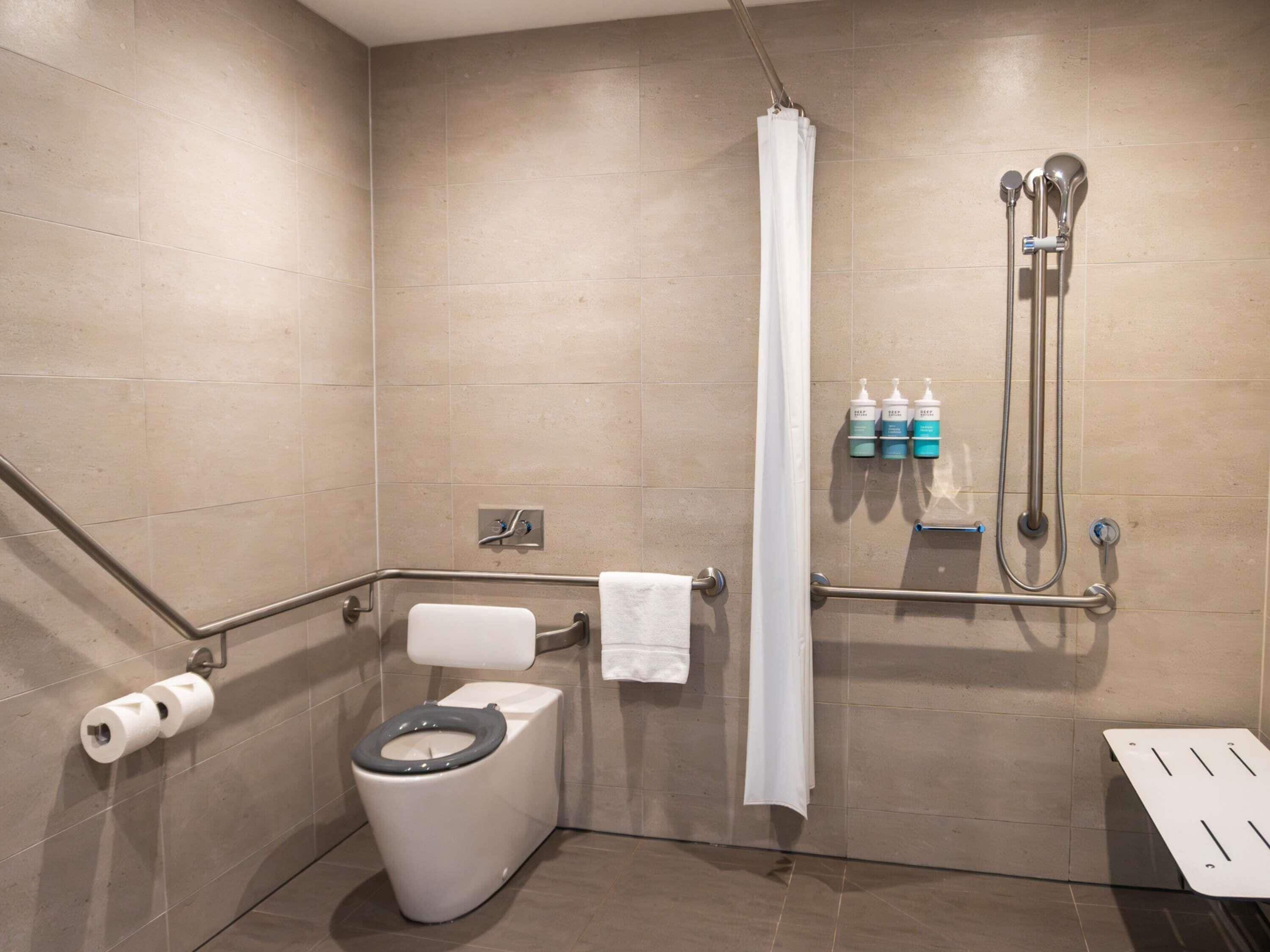 Un baño con inodoro, ducha, barras de apoyo y un perchero para toallas.