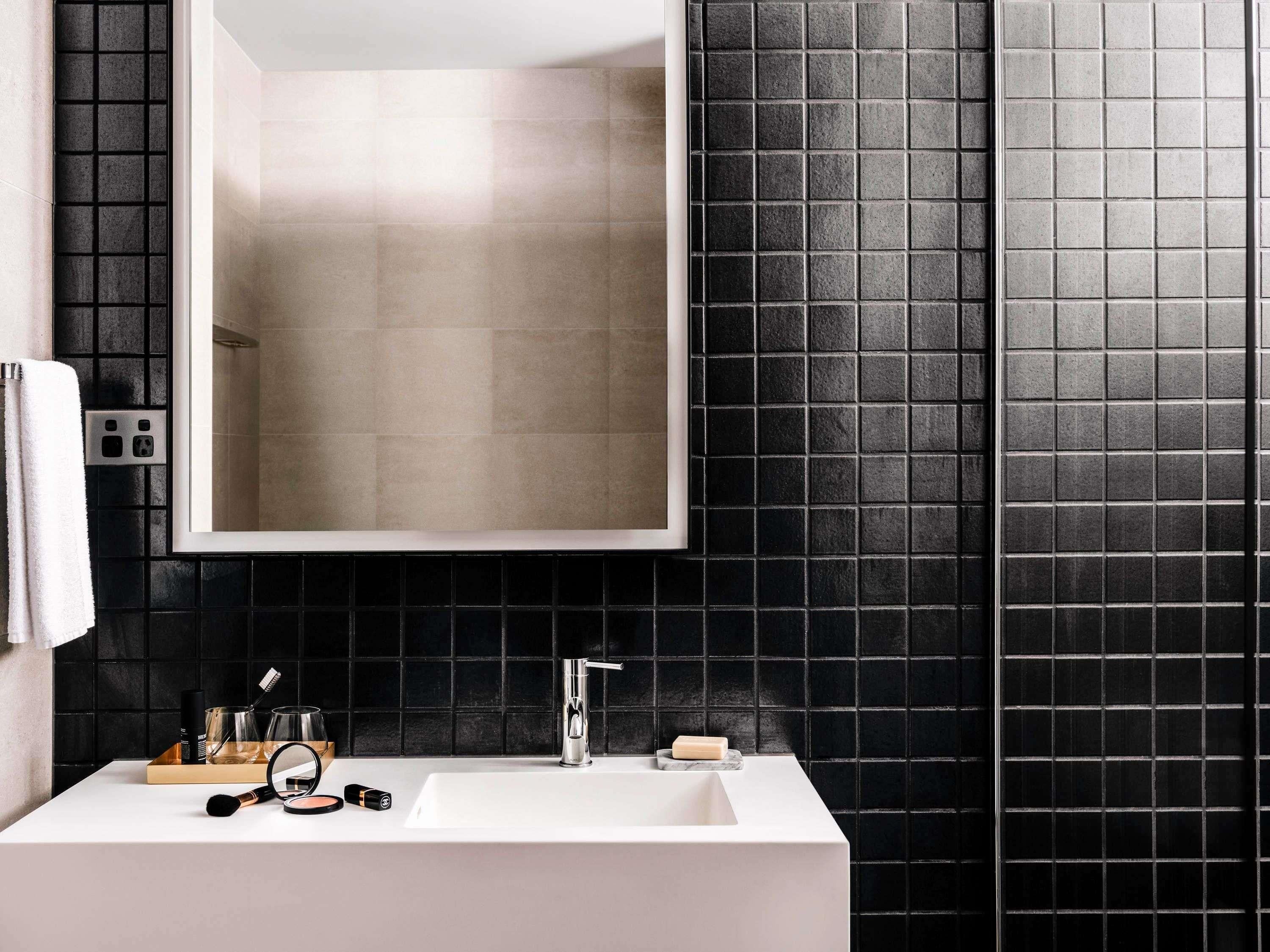 A bathroom with a white sink, a mirror, and black tiled walls.
