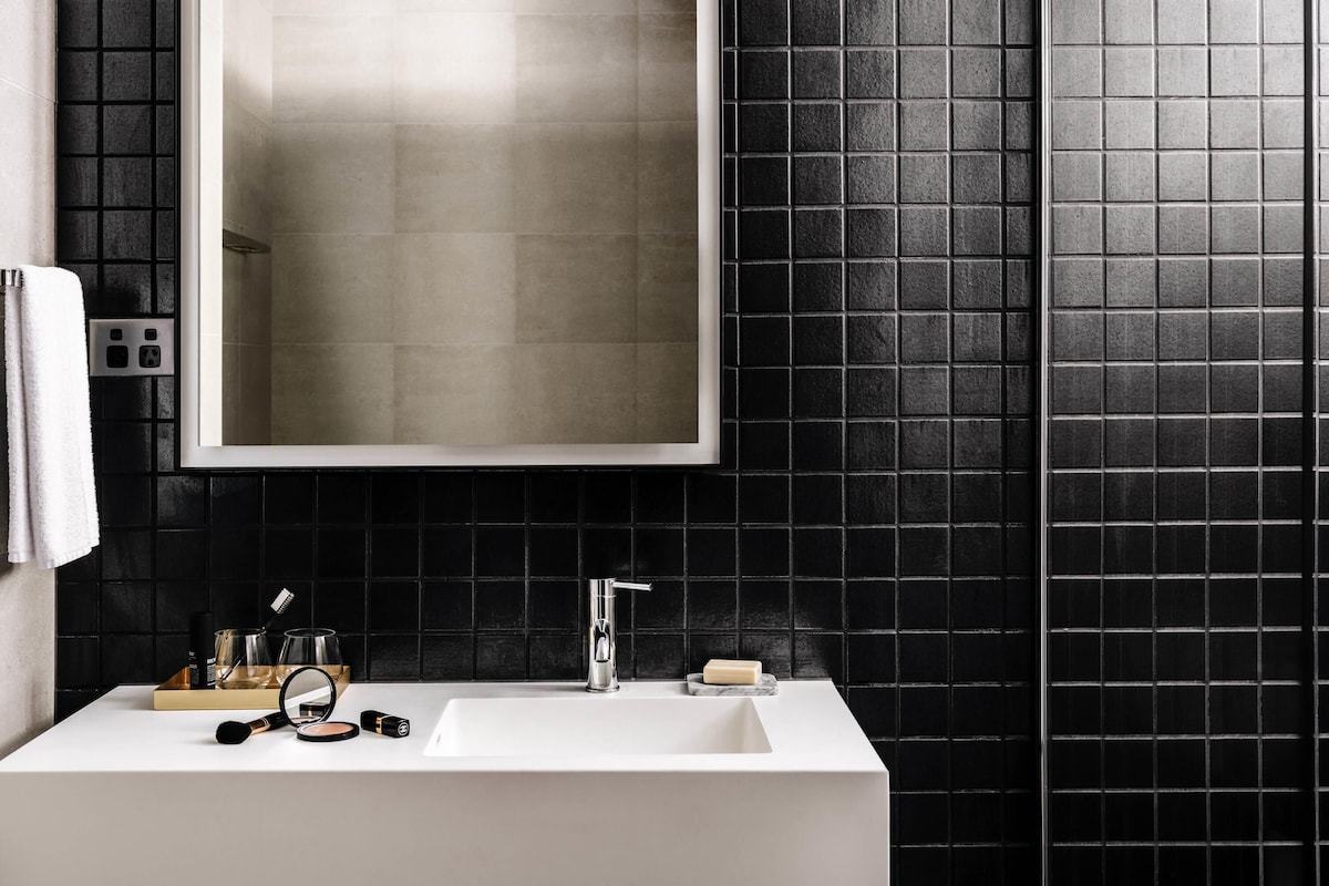 A bathroom with a white sink, a mirror, and black tiled walls.