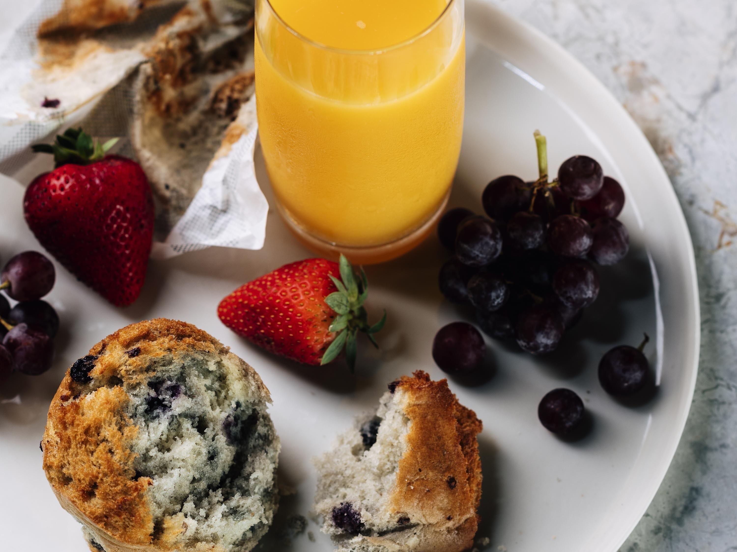 A plate with a muffin, strawberries, grapes, and a glass of orange juice.
