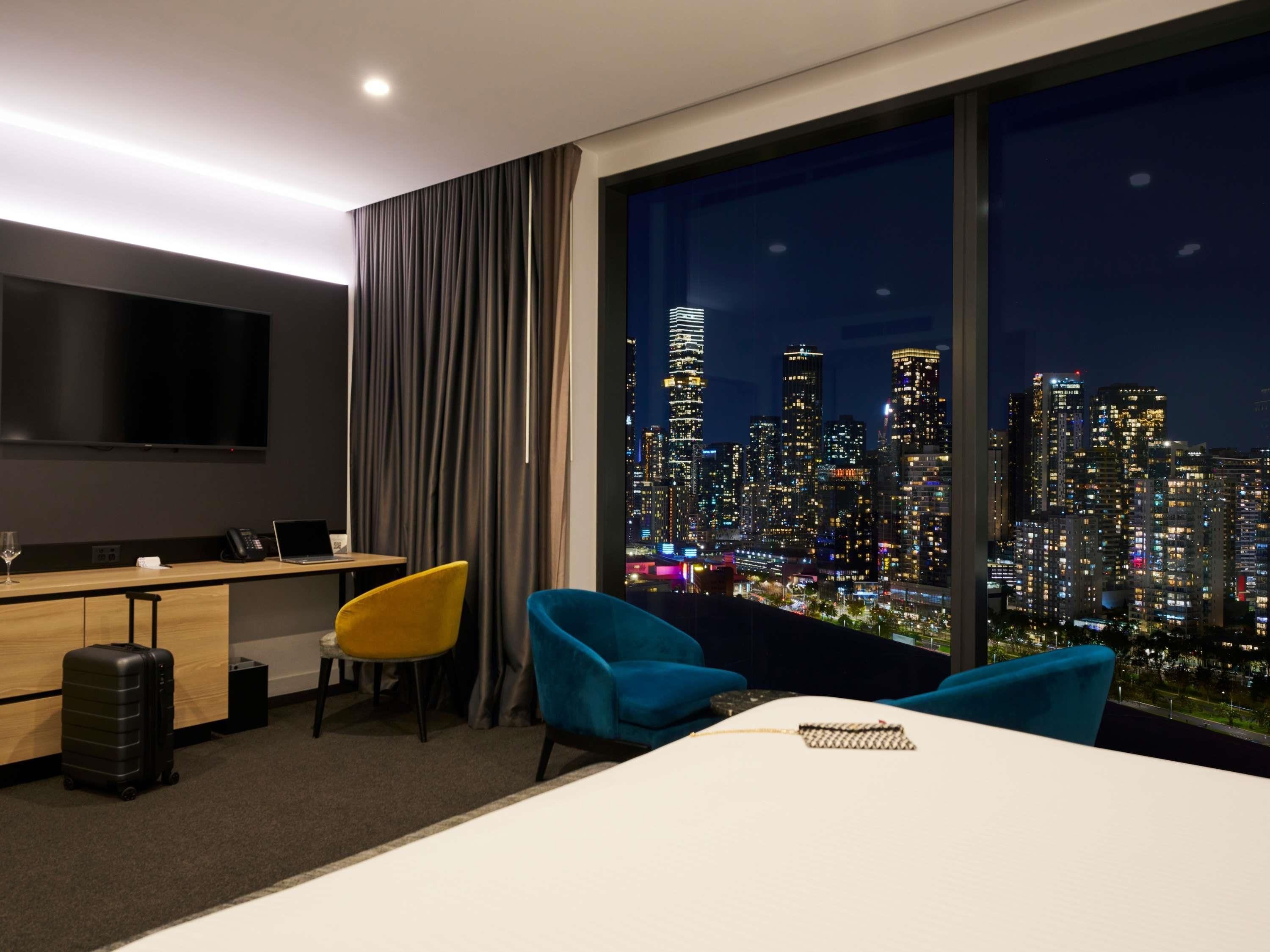 Habitación de hotel con vista a la ciudad, un escritorio, un televisor, una cama y dos sillas.