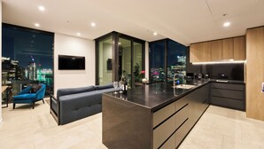 A modern kitchen with a central island, a seating area with a sofa, and a city view through large windows.