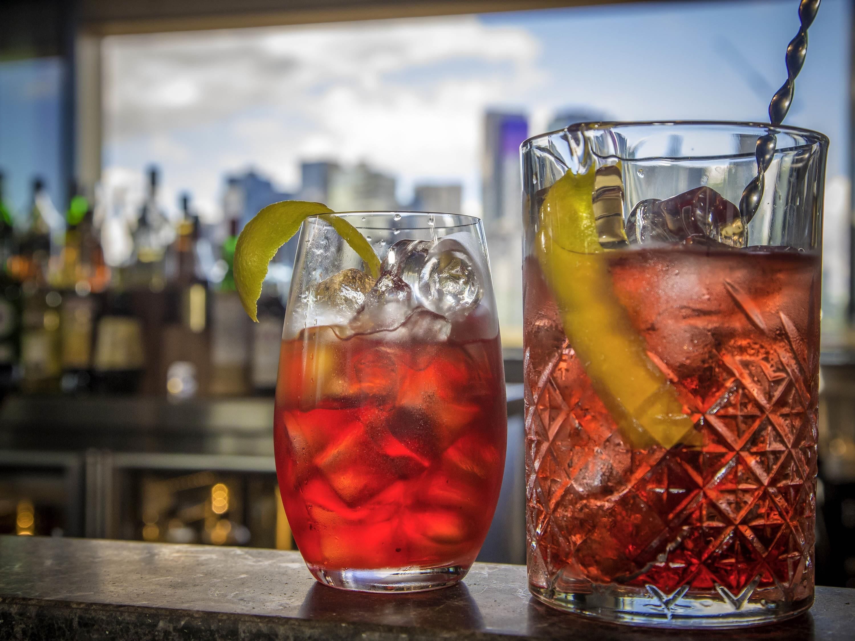 Dos vasos de bebidas rojas con hielo y adornos sobre una barra.