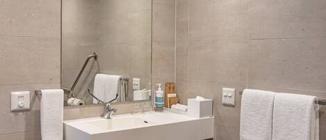 A modern bathroom with a large mirror, white sink, and two towels.