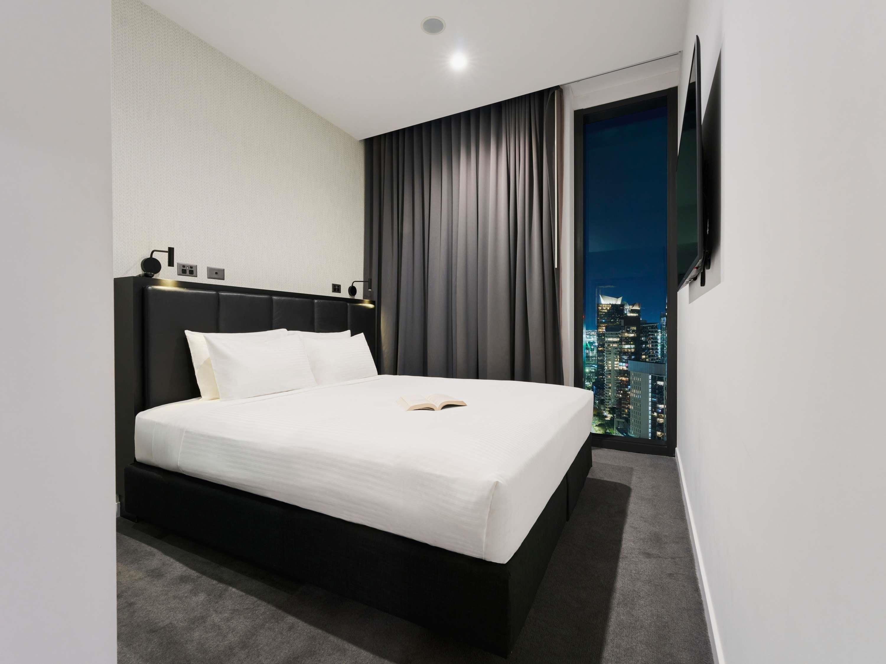 A hotel room with a bed, a city view, a flat-screen TV, and a window with curtains.