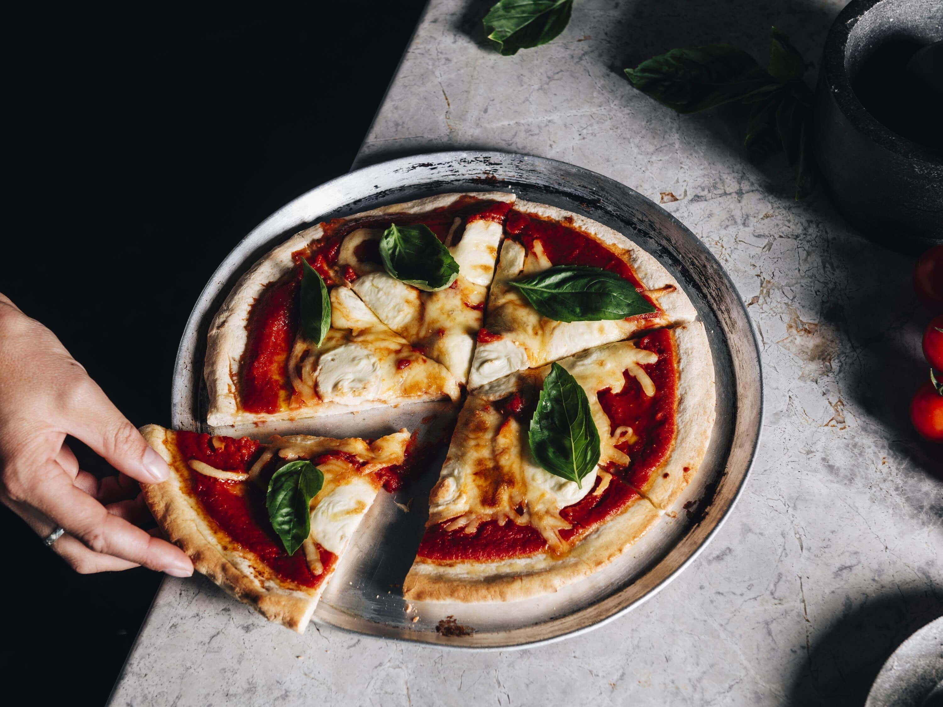 Pizza mit Käse und Basilikumblättern auf einer Metallplatte.