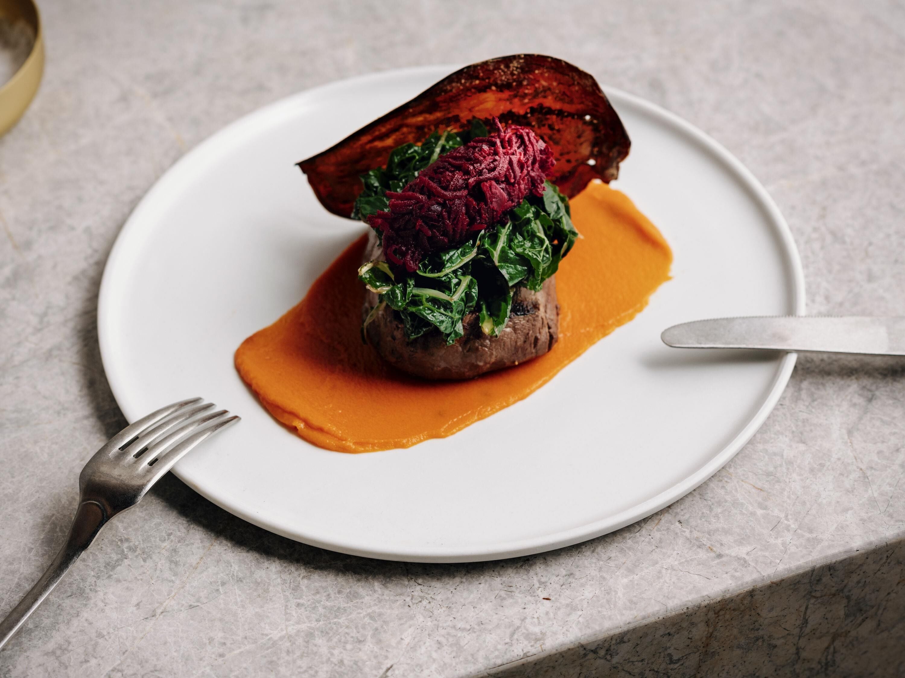 Une assiette blanche contenant un plat de viande, des légumes verts et une betterave.