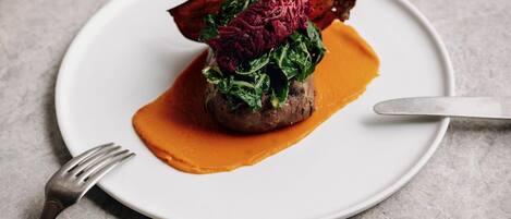Une assiette blanche contenant un plat de viande, des légumes verts et une betterave.