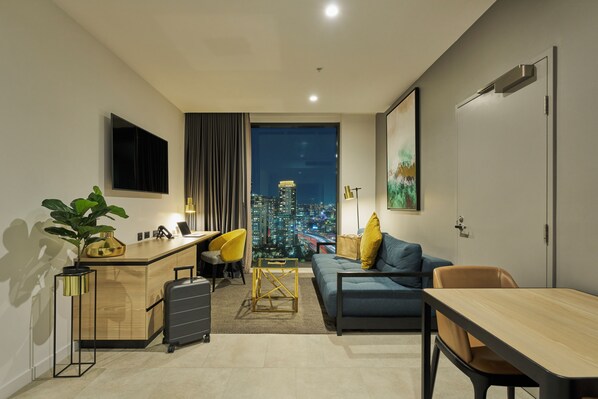 Ein modernes Hotelzimmer mit Blick auf die Stadt, ein Schreibtisch mit Stuhl, eine Sitzecke und ein Esstisch.