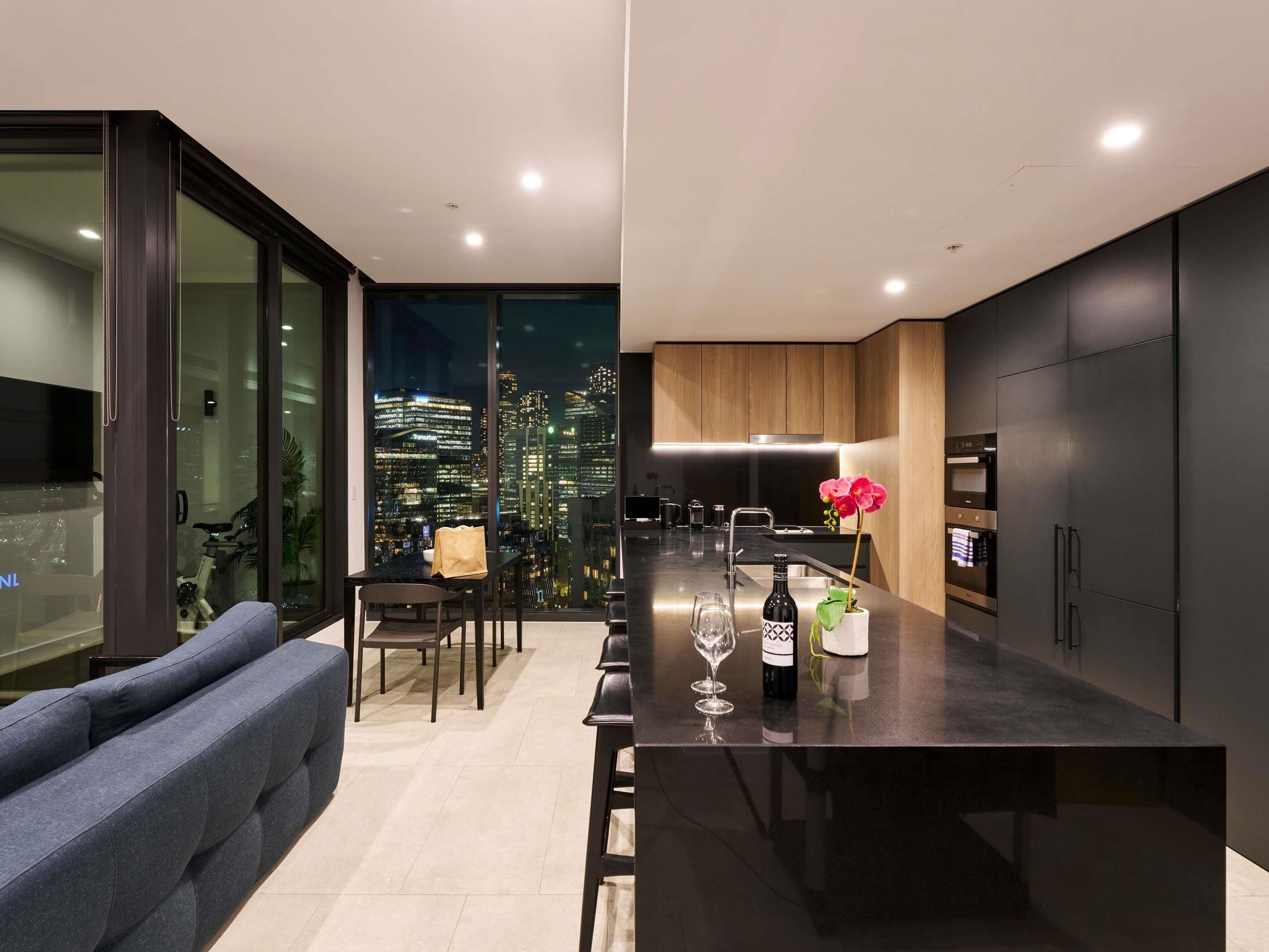 A modern kitchen with a city view, a dining area with a sofa, and a bar area with a wine bottle and glasses.